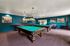 Inviting recreation room featuring two elegant billiard tables, vibrant blue walls, and charming vintage artwork, ideal for entertainment.