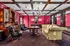 Elegant living area with vintage charm featuring ornate wood accents, plush seating, and a grand chandelier against rich, red damask wallpaper.