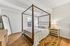 Elegant bedroom with a cozy four-poster bed, stylish furnishings, and a full-length mirror, bathed in natural light for a serene ambiance.