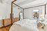 Elegant bedroom with a cozy four-poster bed, chic wooden dresser, and a large mirror, offering a blend of modern and rustic charm with ample natural light.