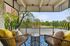 Dog-Friendly Apartments in Speer, CO - El Greco Apartments - Covered Balcony With Woven Lounge Chairs, Blue Patterned Outdoor Rug, Small Side Table, and Scenic Tree and City Views.