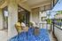 Speer, CO, Pet-Friendly Apartments - El Greco Apartments - Private Balcony Seating Area With Blue Outdoor Rug, Sliding Glass Door Entry, Textured Stucco Walls, and Views of Nearby Trees.