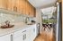 Modern kitchen with wood cabinets, elegant backsplash, and stainless steel appliances leading to a bright dining area with outdoor view.