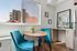 Charming dining nook with vibrant turquoise chairs and wooden table, featuring a large window with cityscape views.