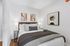 Cozy bedroom with modern decor, featuring a plush bed with decorative pillows and stylish abstract artwork on white walls.