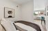 Inviting bedroom with modern decor and comfortable bedding, featuring a cozy seating area near large sunlit windows.