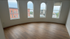 Bright and spacious room with elegant arched windows offering urban views, featuring sleek hardwood flooring for a modern touch.