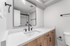 Modern bathroom with sleek black fixtures, a large mirror, wooden cabinetry, and a pristine white countertop.