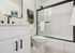 Modern bathroom with sleek white cabinetry, large mirror, and glass-enclosed shower. Elegant black fixtures and contemporary artwork add style.