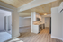 Open and airy apartment kitchen with modern stainless steel appliances, sleek white cabinetry, and beautiful wooden ceiling. Abundant natural light flows through large sliding glass doors.