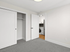 Bright and modern bedroom featuring a spacious closet, plush gray carpet, and a glimpse into a stylish kitchen with sleek appliances.