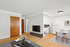 Bright and airy living area with elegant wood flooring, modern TV setup, and cozy dining space next to a compact kitchen.