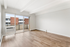 Bright and spacious living room with sleek wooden flooring, large window, and balcony access, ideal for contemporary living.