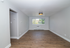 Bright, spacious living room with elegant wood flooring and a large window offering lush, green views.