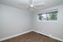 Bright, modern bedroom with sleek wooden floors, a large window, and an elegant ceiling fan in a serene apartment setting.