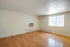 Bright and spacious room with hardwood flooring, large window with blinds, and wall-mounted air conditioning unit.