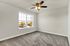 Bright bedroom with large window and ceiling fan, featuring neutral walls and plush carpet.