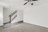 Bright living room with plush carpet, modern ceiling fan, and elegant staircase leading to the upper level.
