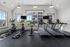 Bright and modern apartment gym with large windows, featuring elliptical machines, stationary bikes, and treadmills.