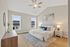 Elegant bedroom with modern decor, featuring vaulted ceiling, large windows, and cozy bedding in a serene setting.