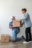 Happy couple moving into their new home, smiling and sharing a moment while handling moving boxes on polished hardwood floors.