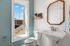 Bright and modern bathroom with a large window, sleek pedestal sink, and stylish wooden framed mirror.