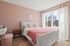 Cozy bedroom with soft pink walls, large window with sheer curtains, and stylish decor.