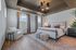 Elegant master bedroom with large windows, chic chandelier, and stylish decor, featuring a cozy armchair and a sophisticated neutral palette.