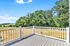 Inviting balcony with sleek white railing offering breathtaking views of lush green trees and serene open fields under a clear blue sky.