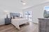 Bright and modern bedroom featuring a plush bed with elegant lighting, wood flooring, and large windows offering a serene view.