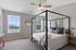 Bright and airy bedroom featuring a stylish canopy bed, modern ceiling fan, and scenic window views.