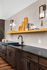 Modern kitchen with dark cabinetry, sleek black countertop, and open shelving featuring decorative items and cookbooks.