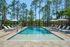 Inviting outdoor pool area surrounded by lush trees, featuring comfortable lounge chairs and shaded umbrellas for ultimate relaxation.