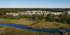 Scenic aerial view of modern apartment complex nestled in lush greenery with a serene waterfront and boardwalk, offering a harmonious blend of nature and urban living.