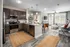 Open-concept living and kitchen area with modern appliances, wooden cabinets, granite countertops, and two jute rugs on hardwood flooring. A cozy seating area with large windows at Abberly Liberty Crossing Apartments in Charlotte, NC