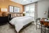 A comfortable bedroom featuring a cozy bed with plush bedding, a nightstand with a lamp, and a large window allowing natural light to fill the room at Abberly Liberty Crossing Apartments in Charlotte, NC
