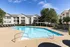 Outdoor swimming pool with a spacious sundeck, surrounded by lounge chairs, a pergola-shaded seating area, and landscaped greenery, with apartment buildings in the background at Abberly Woods Apartments in Charlotte, NC