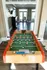 Community game room featuring a foosball table with a view into a seating area with tall chairs, a mounted TV, and large windows providing natural light at Abberly Woods Apartments in Charlotte, NC
