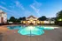Illuminated swimming pool with a luxurious patio area during dusk, featuring lounge seating and a grand clubhouse with bright arched windows and columns at Abberly Woods Apartments in Charlotte, NC