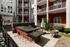 An outdoor patio with a firepit and tables and chairs in front of an apartment building at Abberly Noda Vista Apartments in Charlotte, NC