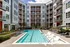 An outdoor swimming pool with lounge chairs and umbrellas in front of an apartment building at Abberly Noda Vista Apartments in Charlotte, NC