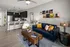 A living room with a blue couch and coffee table, and a kitchen in the background at Abberly Noda Vista Apartments in Charlotte, NC