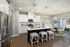 A kitchen with white cabinets, a large island with three stools, and granite countertops at Abberly Alston Townhomes in Cary, NC