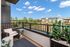 Charming balcony view with cozy seating and lush greenery overlooking a modern apartment complex and blue sky.