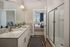 Modern bathroom with granite countertop, sleek dual sinks, and a spacious glass shower, leading to a cozy, well-lit bedroom with stylish decor.