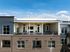 Modern apartment exterior view with stylish balcony and large glass doors, set against a bright blue sky.