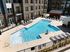 Luxurious apartment complex featuring a sparkling pool with elegant lounge chairs, surrounded by modern buildings and a vibrant sunset sky.