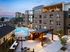 Modern apartment complex with elegant swimming pool and illuminated patio area, surrounded by lush greenery and stylish architecture.