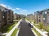 Modern apartment complex with sleek architecture, lush greenery, and ample parking under a clear blue sky.