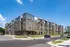 Modern apartment complex with stylish architecture, featuring spacious balconies and surrounded by lush greenery under a clear blue sky.